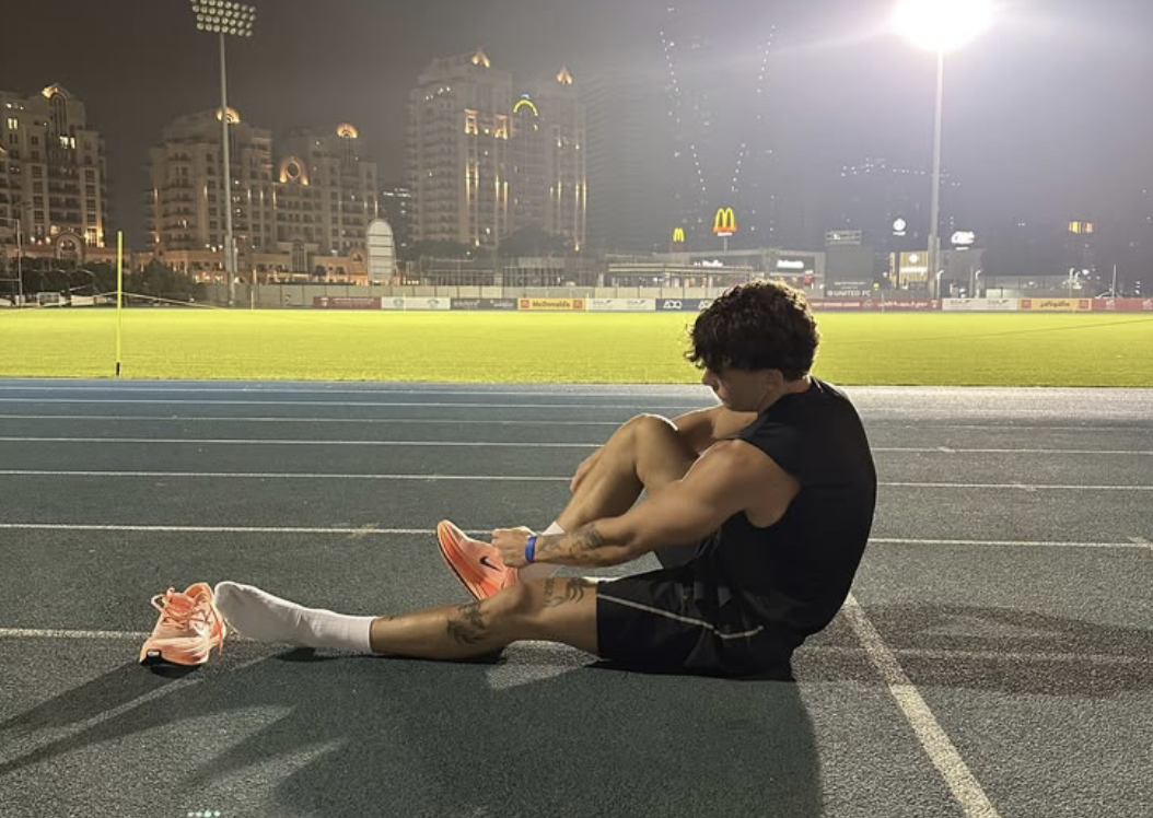 An athlete seated on a floodlit track at night taking a break